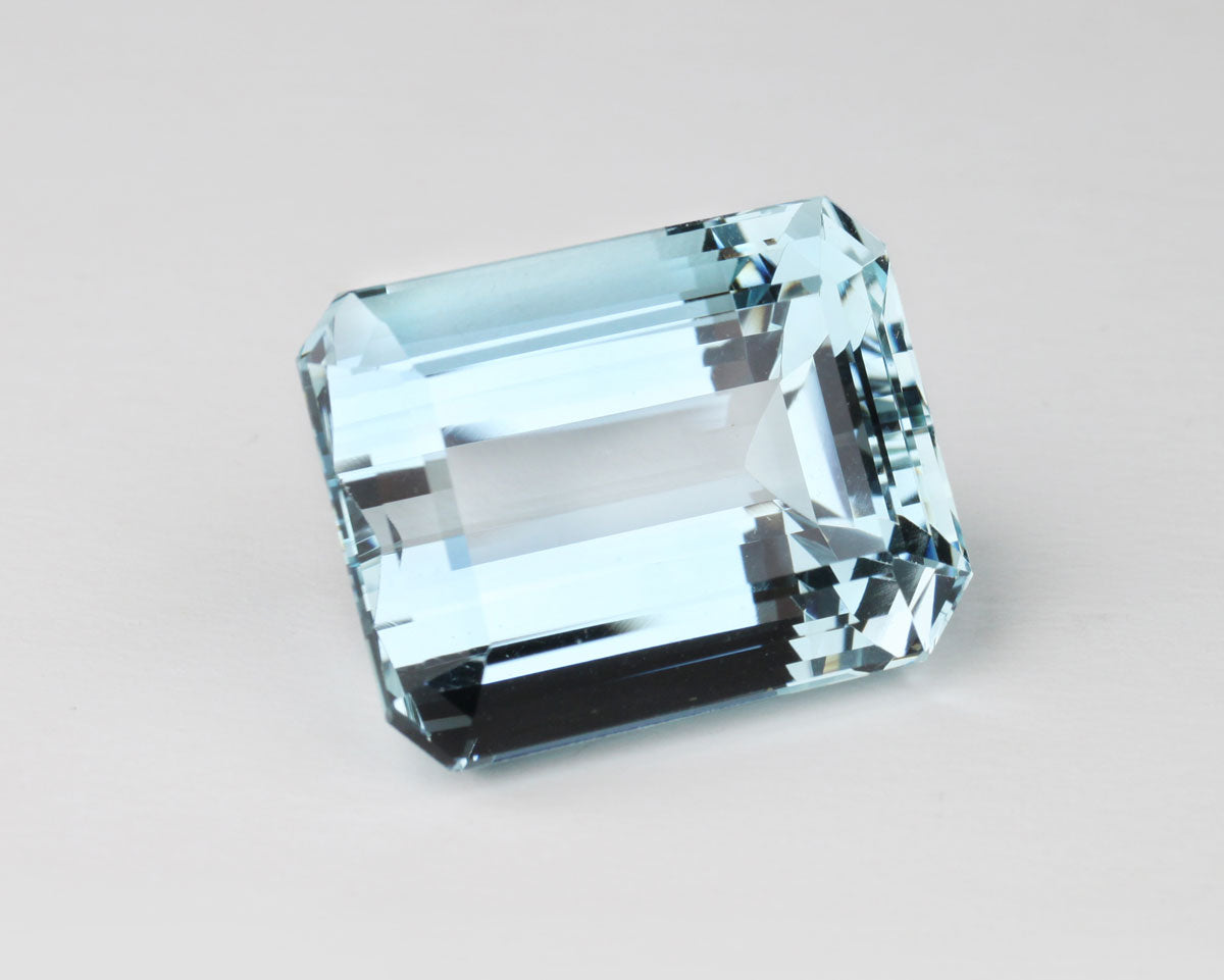 Natural faceted aquamarine gemstone on a light gray background