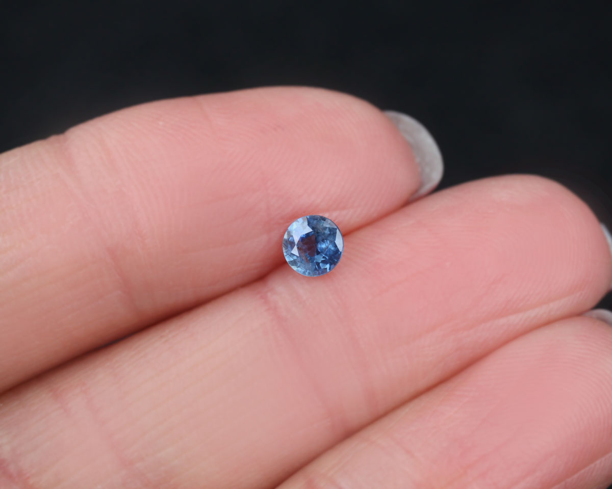 Blue faceted sapphire held between fingers against a dark background