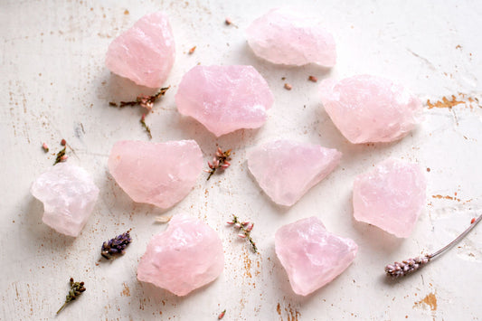 Rough Rose quartz on a textured white surface with lavender flowers.
